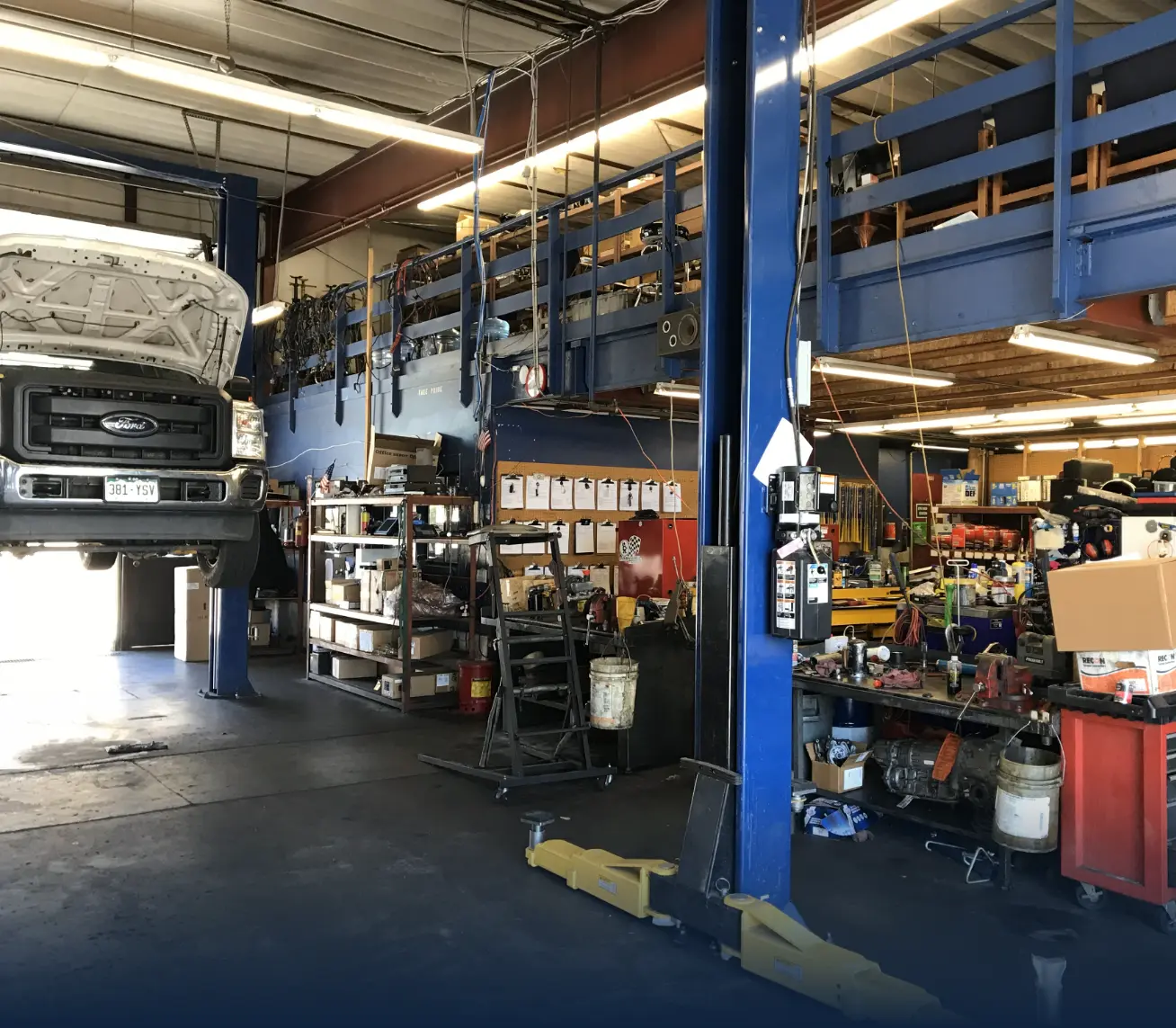image of inside shop bay area where tools and staff rooms are as well as parts area. There is a white ford truck raised on a lift.