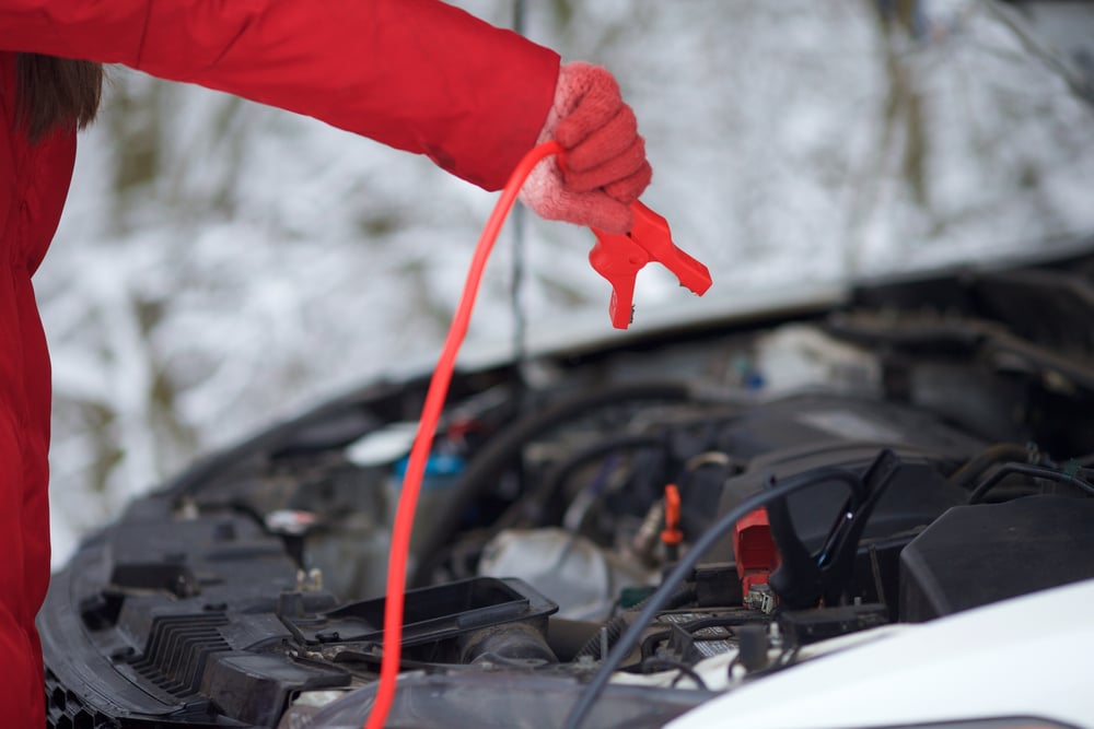 technician using jumper cables on her car battery in the winter for battery maintenance in cold weather | Branch Automotive