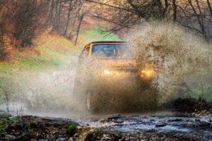 Diesel Power and Durability: How to Prepare Your Diesel Truck for Colorado's Fall Adventures with Branch Automotive. An off-road vehicle traversing a muddy path, with mud splattering as it moves through the challenging terrain.