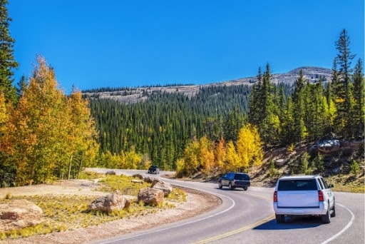 Gas-Powered Truck Road Trips: Get Your Truck Ready for Colorado’s Scenic Fall Drives with Branch Automotive. A vehicle travels along a scenic mountain road, framed by towering trees and distant mountain peaks.