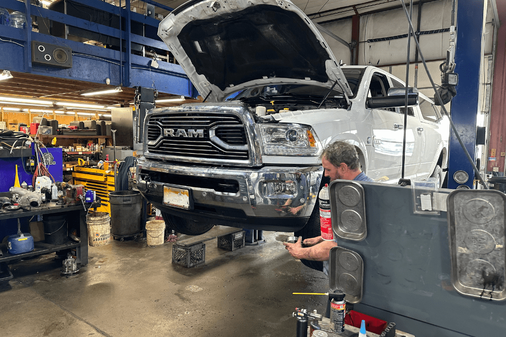 diesel repair costs, diesel repair in Littleton, CO at Branch Automotive. Diesel mechanic working on a white RAM truck lifted in a service bay at an auto repair shop.