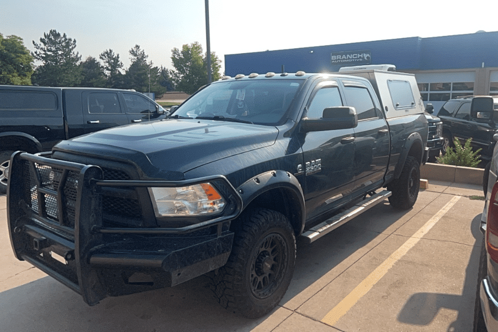 Cummins engine, diesel repair in Littleton, CO by Branch Automotive. Image of a custom lifted black Ram 2500 with off-road tires and a front grille guard, parked outside a busy auto shop.
