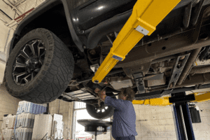 Diesel burning smells, diesel repair in Littleton, CO by Branch Automotive. Image of a technician performing an undercarriage inspection and oil service on a lifted truck, highlighting the shop’s commitment to proper maintenance, safety, and reliable automotive care.