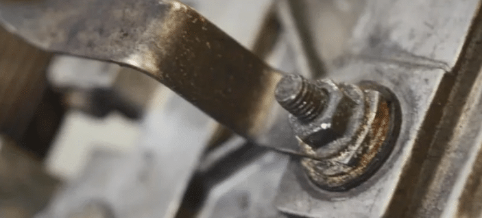 Image of a close-up engine component with a worn grid heater bolt and metal bracket.