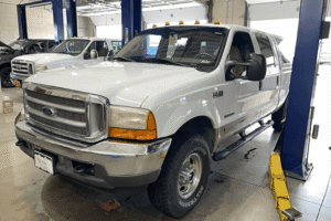 6.7L Powerstroke, diesel repair in Littleton, CO by Branch Automotive. Image of a white Ford Super Duty pickup inside the shop on a lift, ready for service and maintenance by professional diesel technicians.